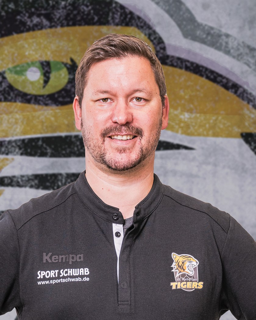 Porträtfoto von Maik im schwarzen Vereinspolo der Waiblingen Tigers, im Hintergrund ein großflächig gemaltes Tigermotiv.